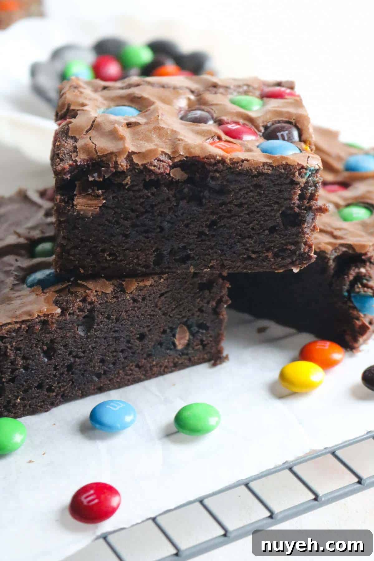 stack of three thick and fudgy m&m brownies with lots of candies sprinkled around them.
