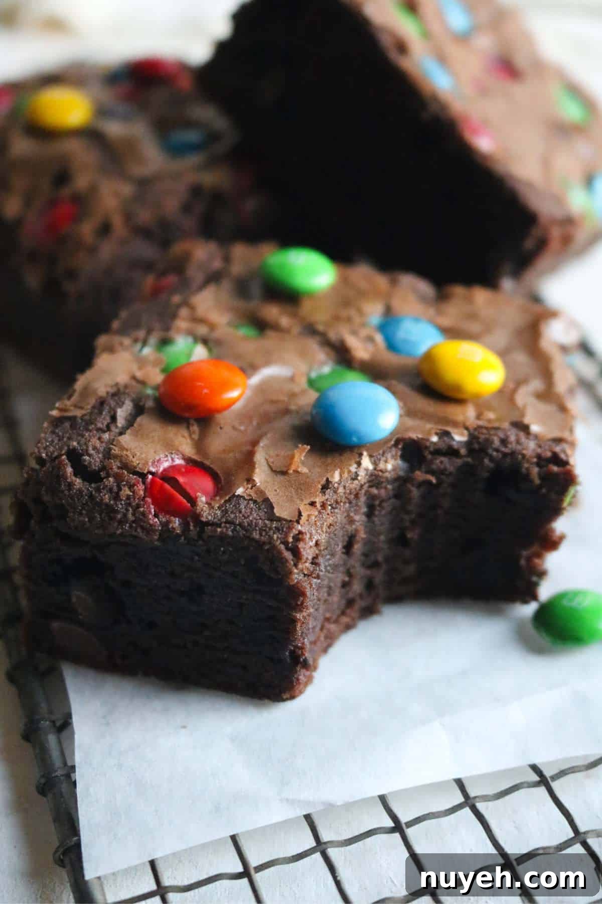 close up view of a thick brownie studded with m&ms with more brownies shingled in the background.