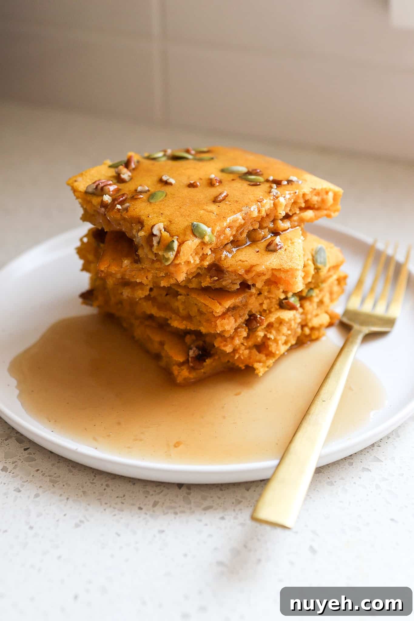side angle of fluffy pumpkin sheet pan pancakes stacked on top of one another on a white plate with gold fork