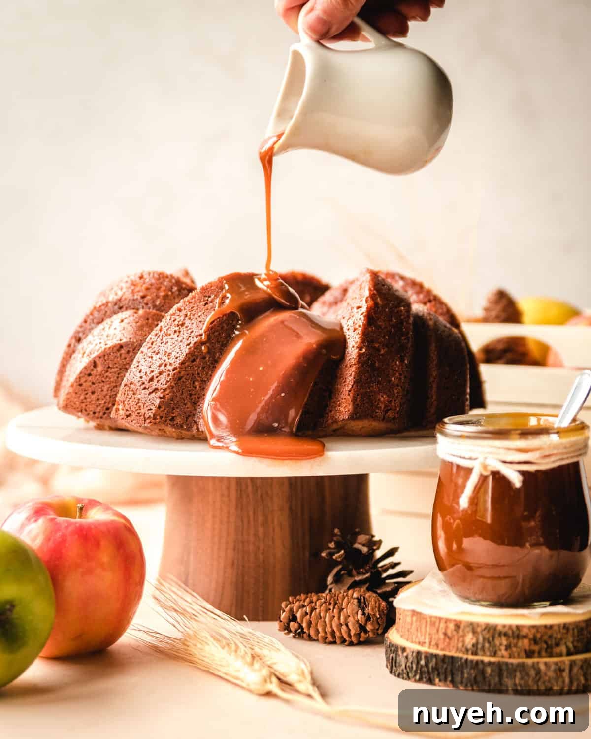 Spiced Apple Cider Bundt Cake with Cinnamon Glaze 2 Apple spice cake on a cake stand with caramel being poured on top.