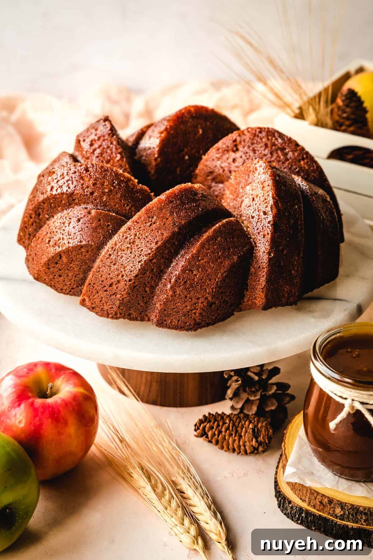 Spiced Apple Cider Bundt Cake with Cinnamon Glaze 3 Beautiful apple spice cake on a cake stand with fall leaves around it.
