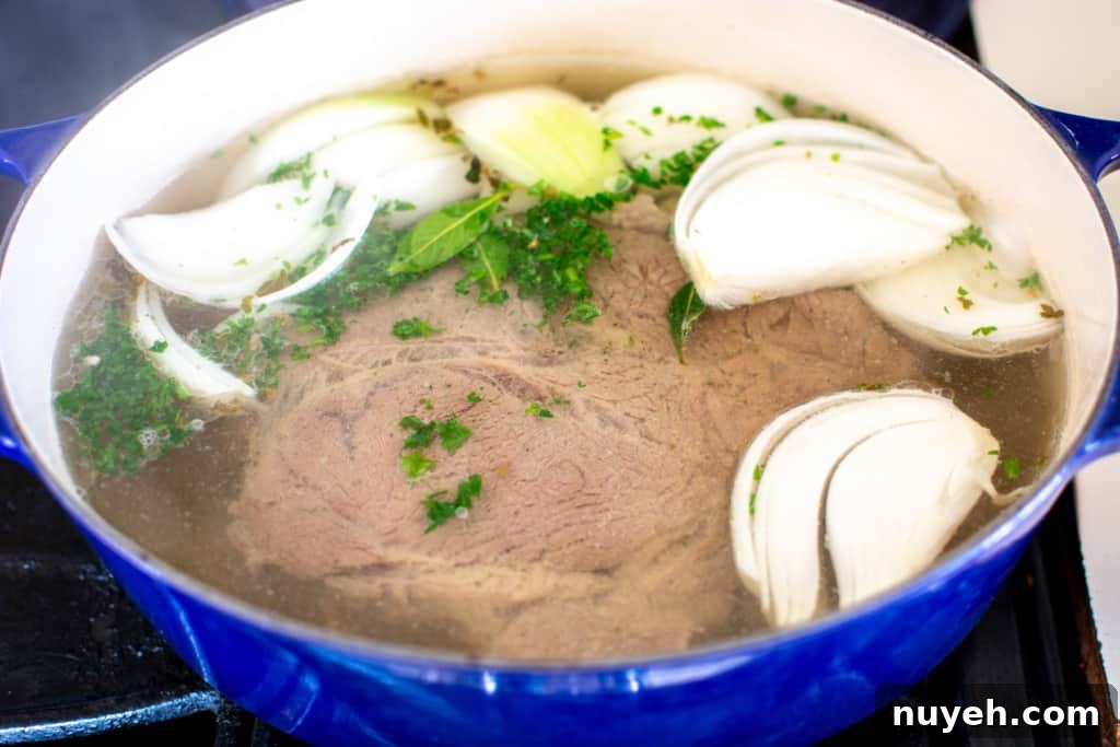 A blue Dutch oven with beef and aromatics.