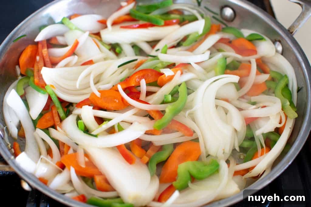 Sliced onions, carrots, and peppers cooking in a pan.