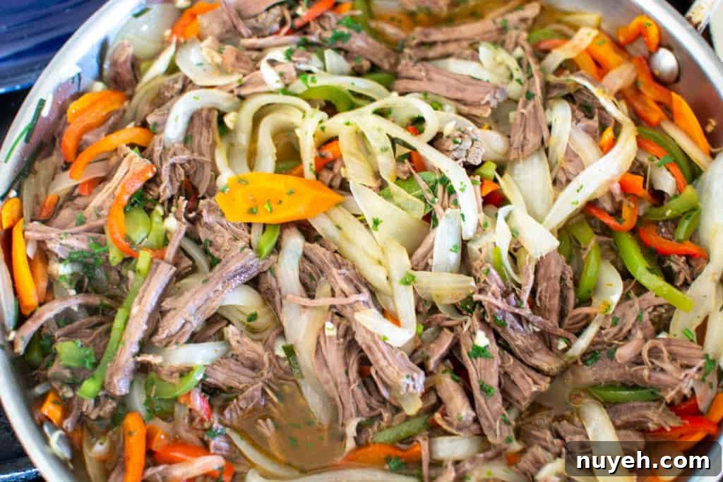 Ropa Vieja in a stainless steel pan with peppers and onions.
