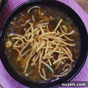 chicken Manchow soup in a black bowl with crispy fried noodles on the top.