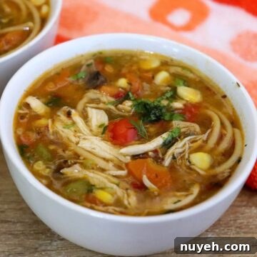 One-pot chicken noodle soup in a white colored bowl placed on a brown counter top.
