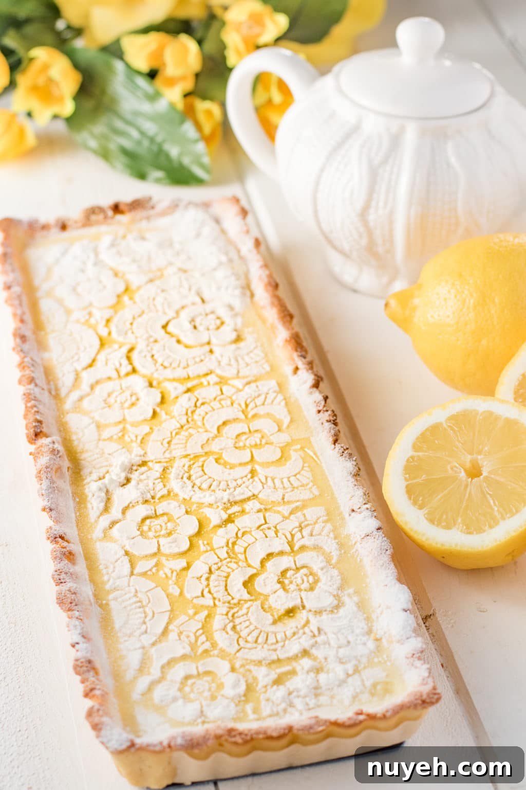 Lemon tart with lemons, flowers and a tea pot on a white background 