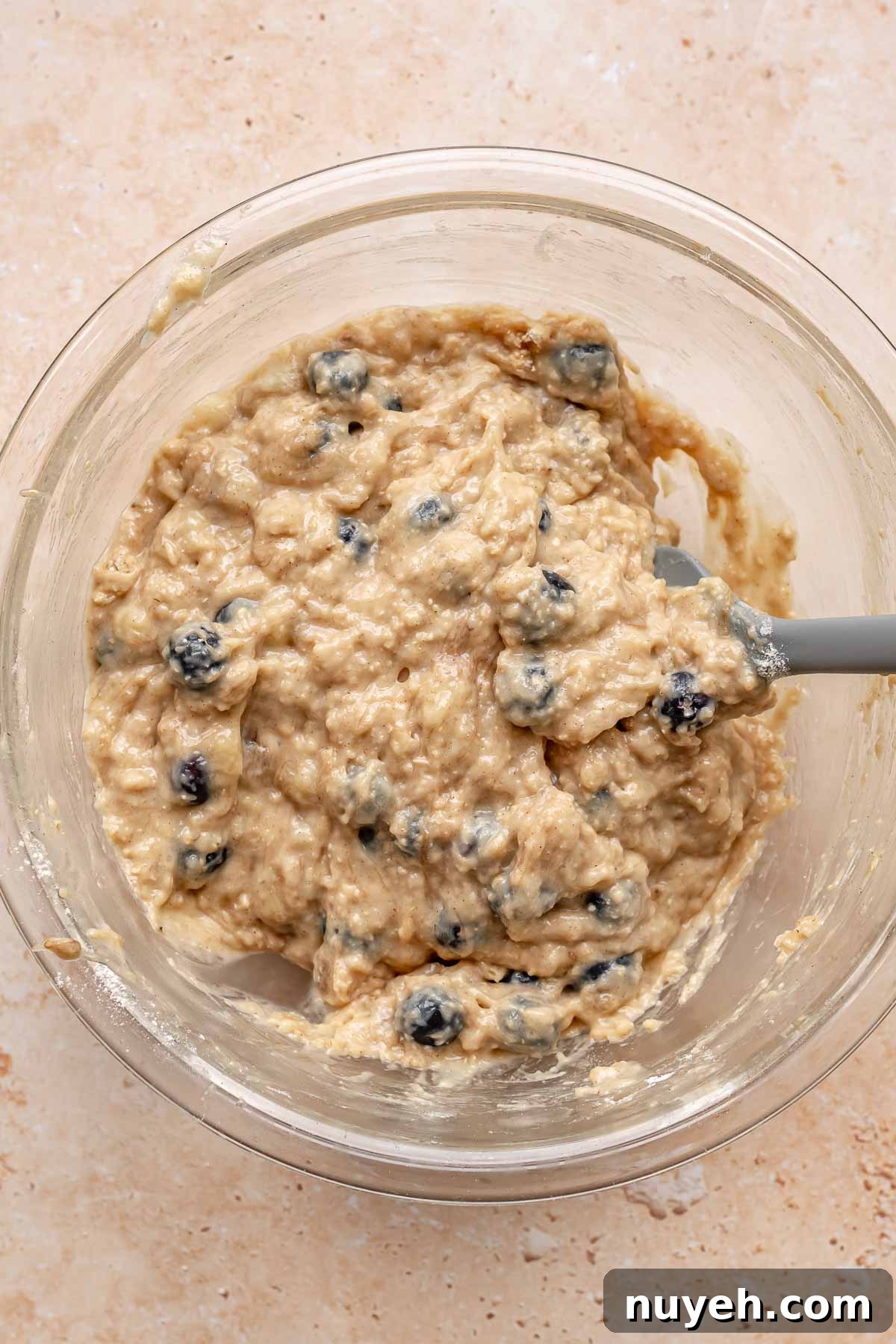 A spatula folds blueberries into muffin batter.