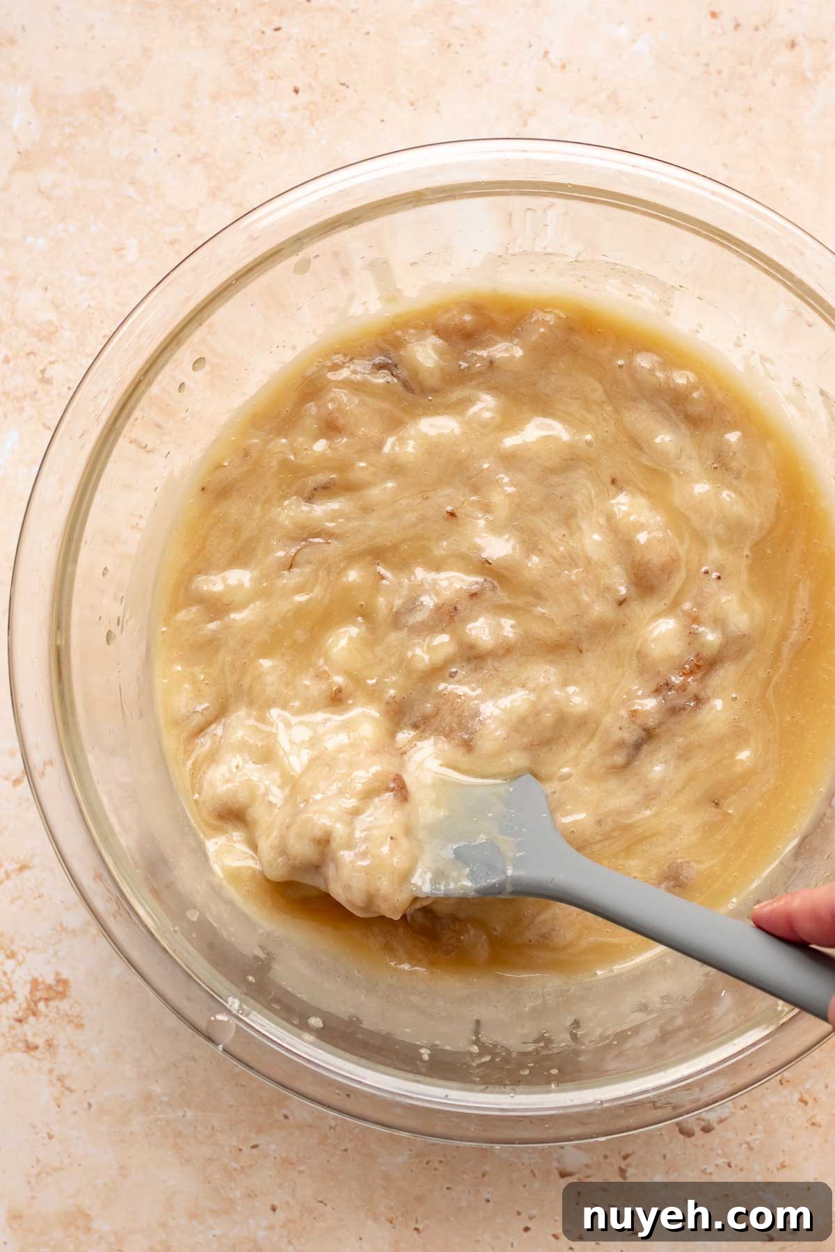 A rubber spatula folds bananas into muffin batter.