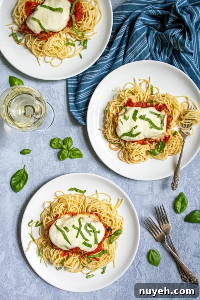 Crispy Oven-Baked Chicken Parmesan with Marinara Sauce 4 Overhead view of three white plate full of spaghetti and topped with Oven Baked Chicken Parmesan showing off melted mozzarella and a fresh basil garnish.