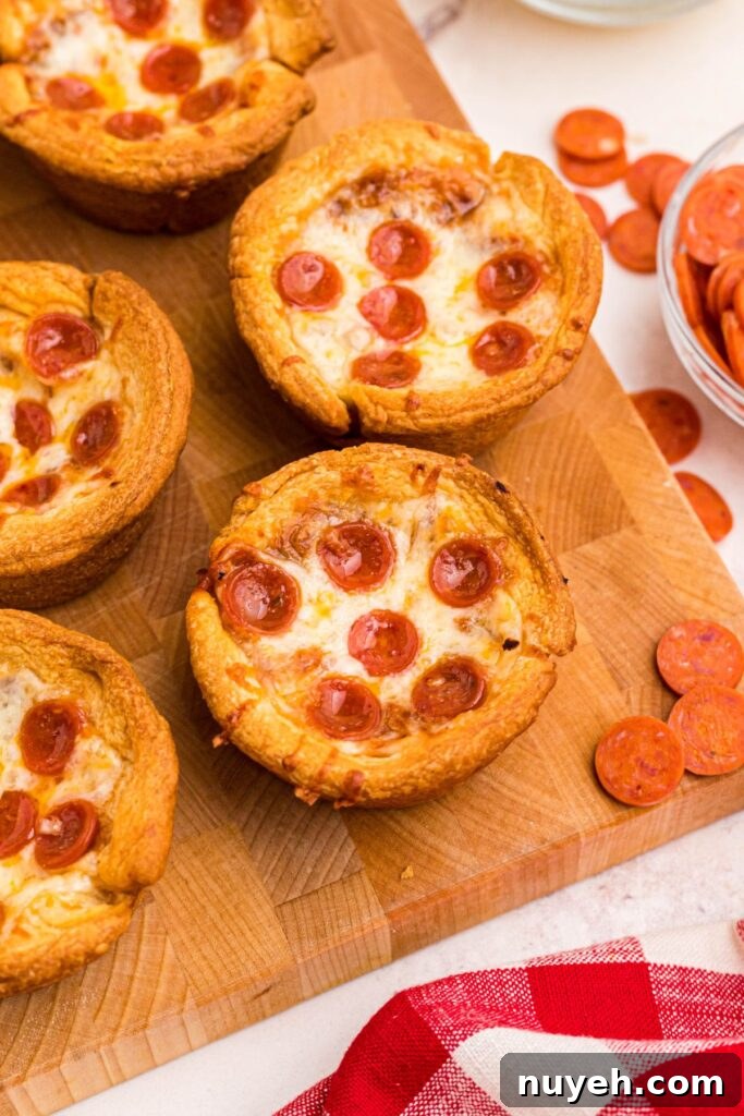 Pizza Cupcakes Recipe: Savory Mini Pizza Bites 2 Golden pizza cupcakes on a wooden cutting board with mini pepperonis scattered around it.