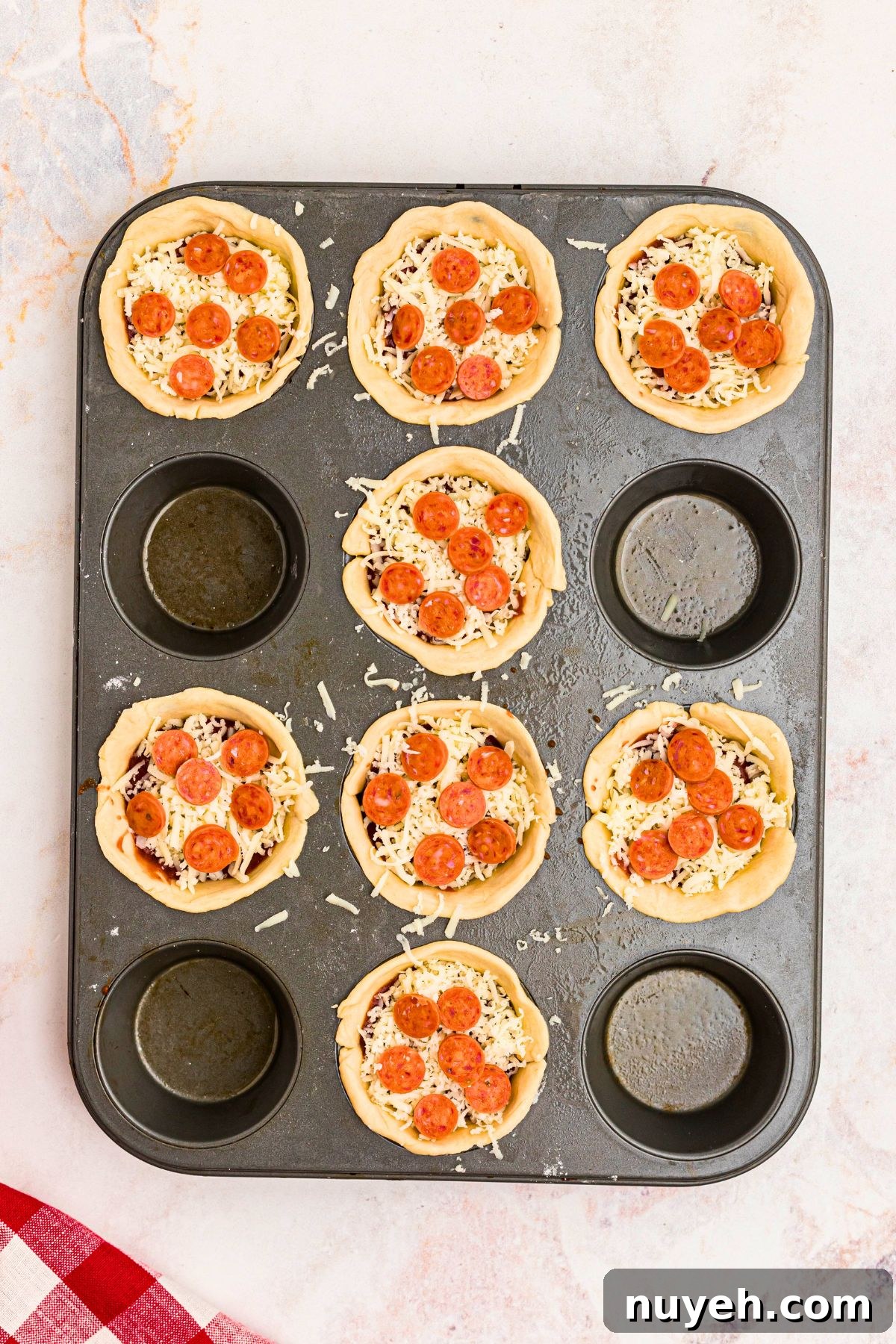 Pizza Cupcakes Recipe: Savory Mini Pizza Bites 5 Muffin tin filled with crust dough, sauce, cheese, and pepperoni before being cooked.