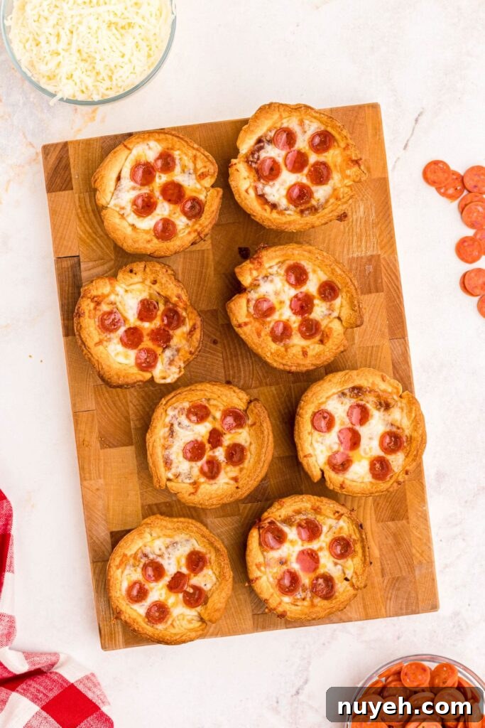 Pizza Cupcakes Recipe: Savory Mini Pizza Bites 6 Golden crispy mini pizza cupcakes on a wooden cutting board, with mini pepperonis scattered on a marble table.