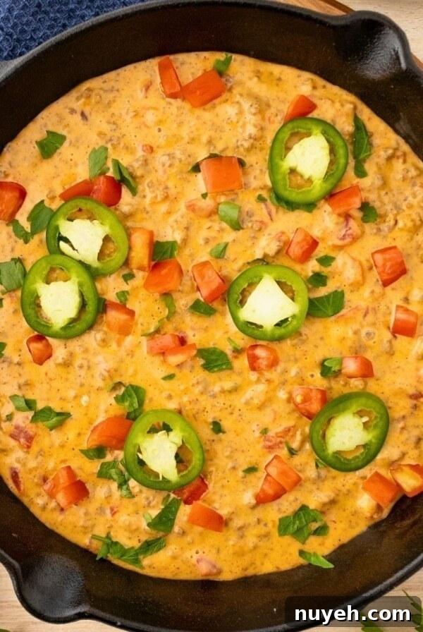 Cheesy Dip in a black skillet, topped with chopped tomatoes and diced jalapenos.