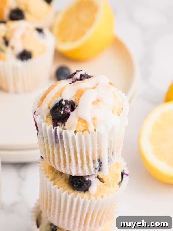 Golden lemon blueberry muffins baked and then stacked on the table with lemons stacked behind the muffins.