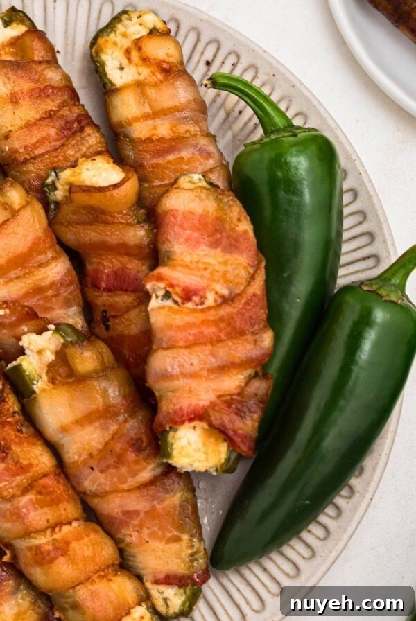 Crispy bacon wrapped jalapenos filled with cheese, stacked on a white plate.
