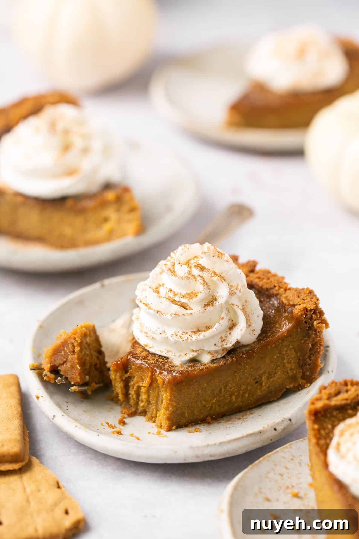 a closeup of a slice of pumpkin pie with a bite taken out on a white plate topped with whipped cream. 