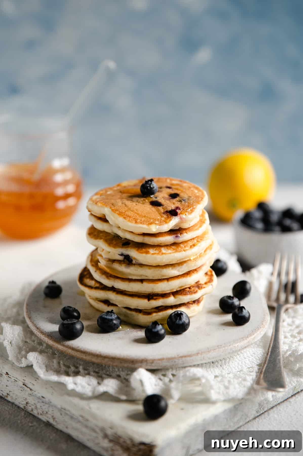 Straight ahead shot of blueberry pancakes on a small plate with glass jar at the back