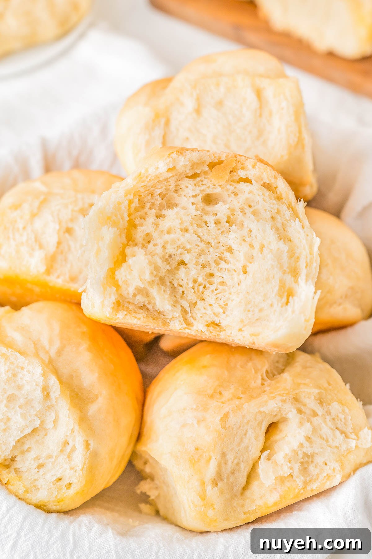 A pile of freshly baked dinner rolls with soft, fluffy interiors, arranged on a white cloth.