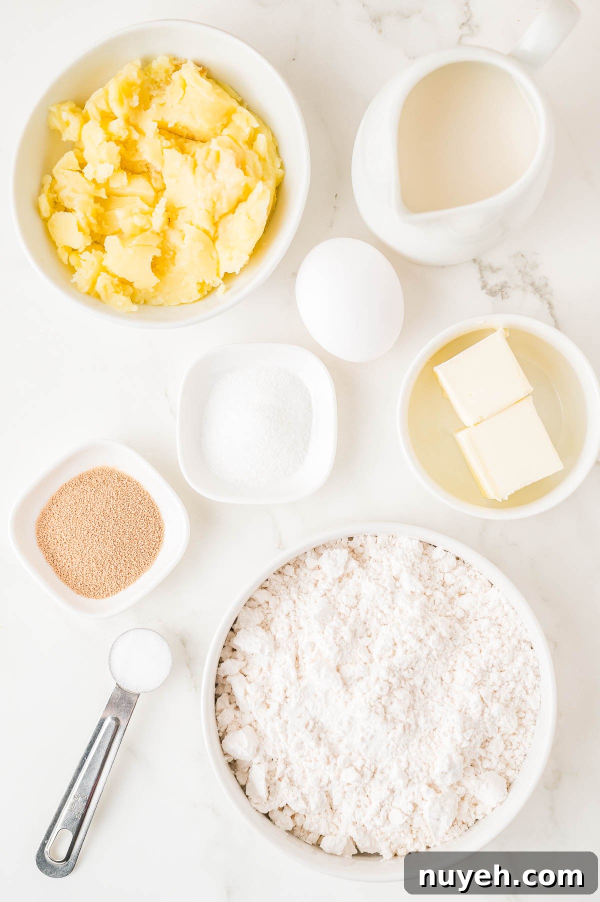 Ingredients on a marble surface: mashed potatoes, cream, egg, butter, flour, yeast, sugar, and salt.