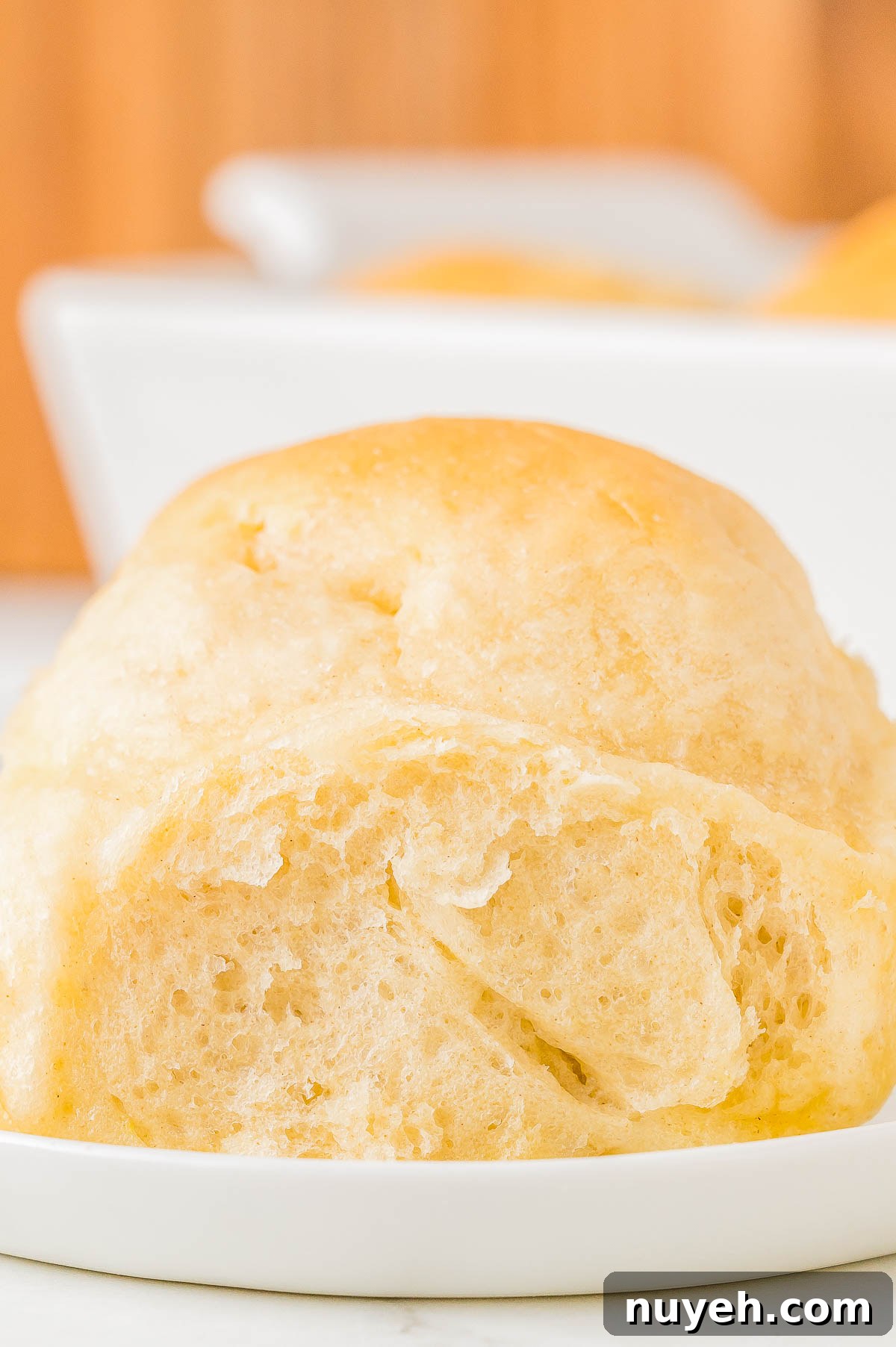 A close-up of a soft, golden-brown dinner roll on a small white plate.