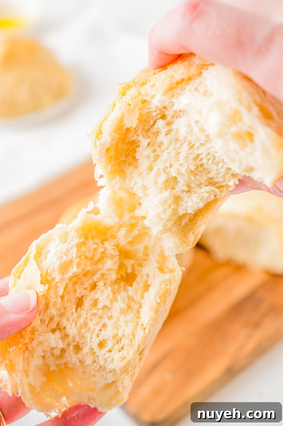 Hands tearing a piece of bread above a wooden cutting board.