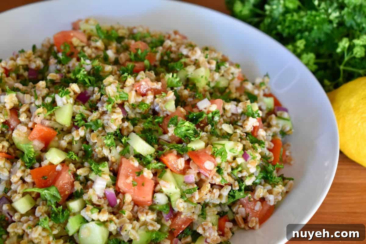 Farro Tabbouleh Salad in a white bowl with lemons next to it. 