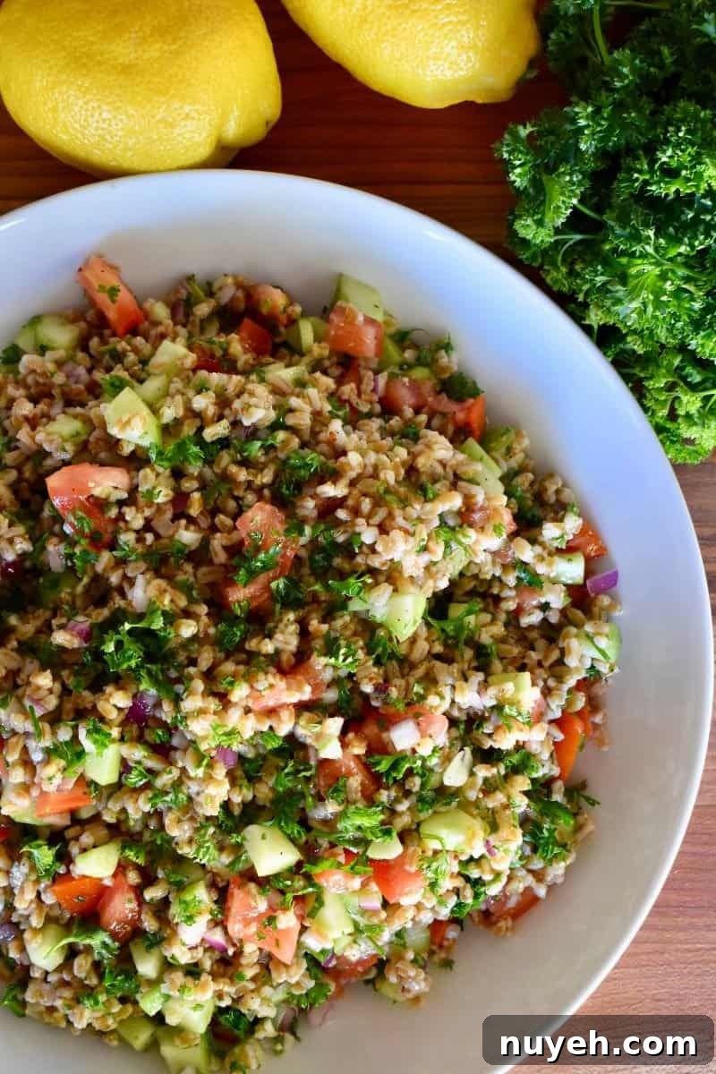 overhead photo of farro tabbouleh salad in a white bowl with lemons and parsley next to it. 