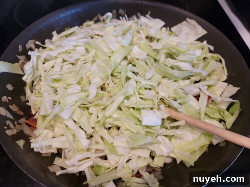 Shredded cabbage in a frying pan with a wooden spoon and bacon