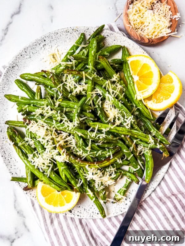 Air fryer green beans on a serving plate with parmesan cheese and lemon wedges.