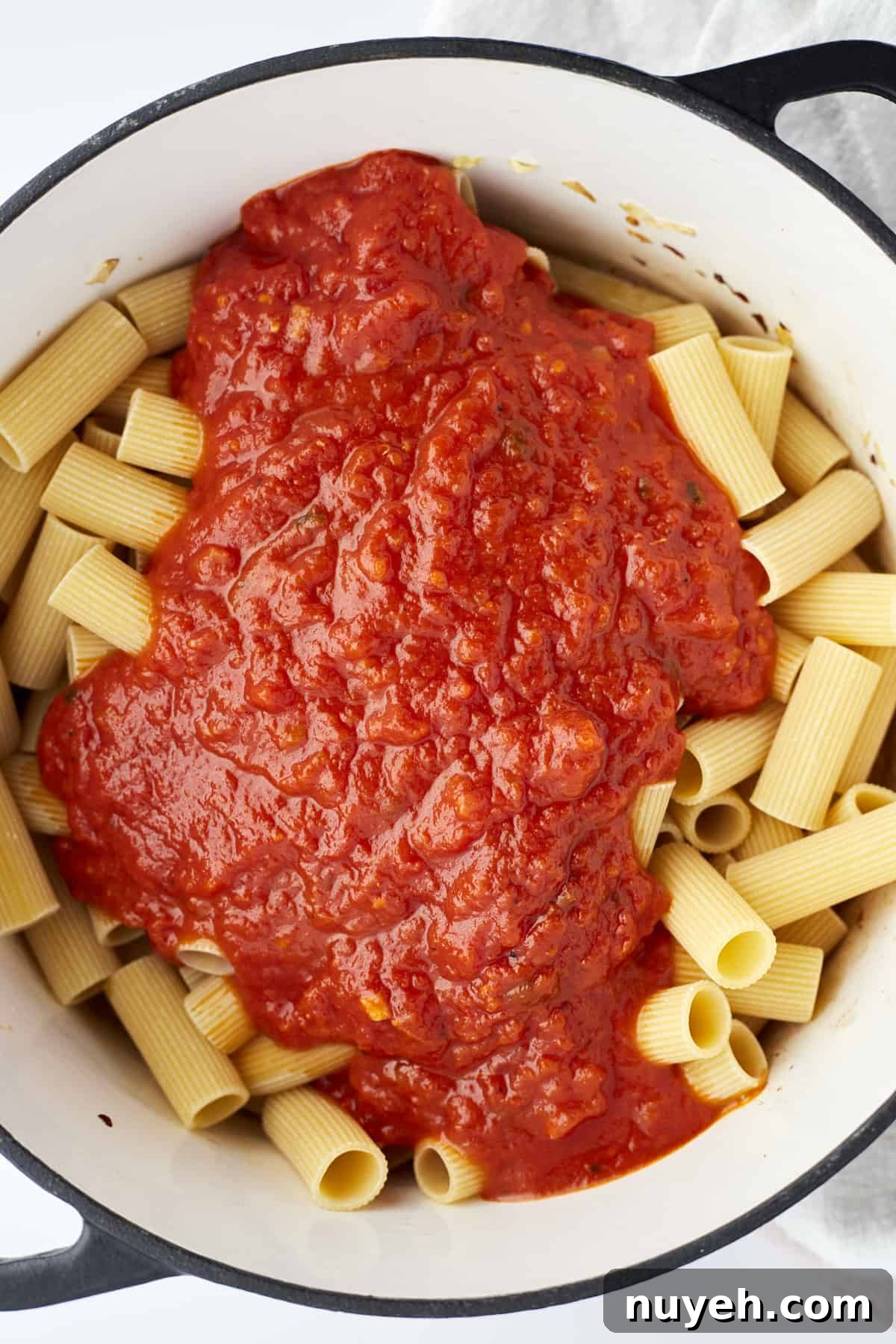 uncooked rigatoni noodles in a pot topped with marinara
