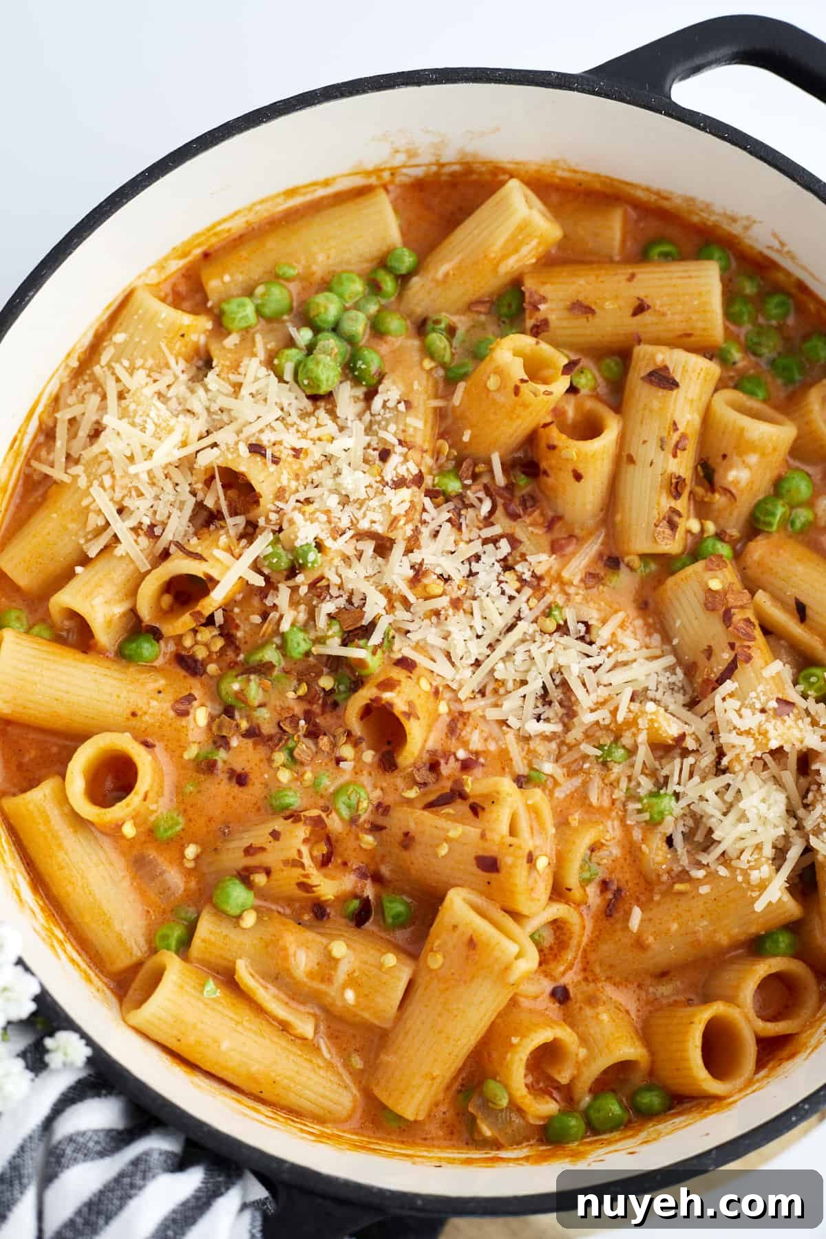 overhead image of a pot of spicy rigatoni with peas topped with shredded Parmesan