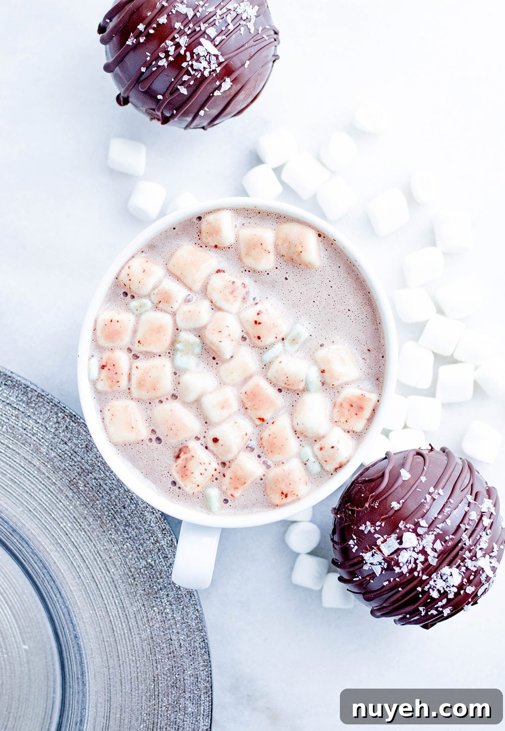 a mug filled with hot cocoa and marshmallows with two salted caramel hot cocoa bombs on the side.