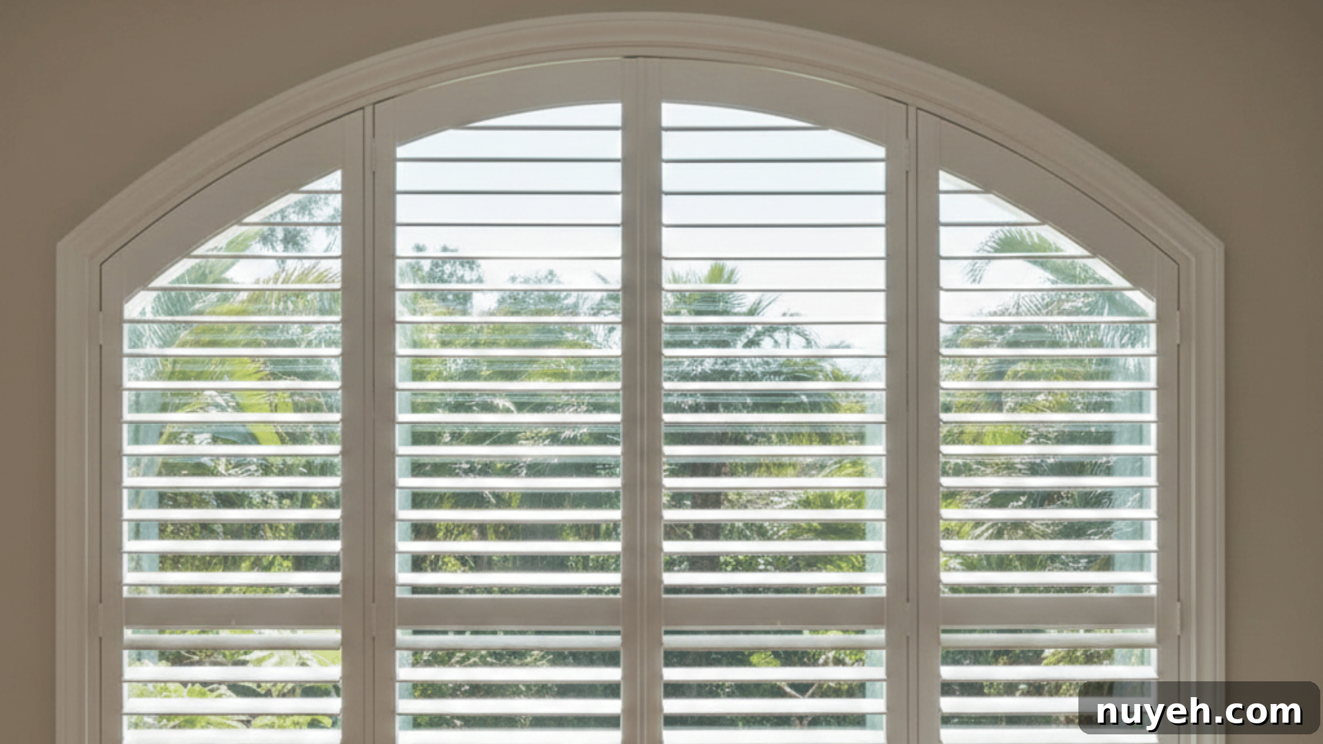 Shutters vs Blinds: Which Window Treatment Fits Your Home? 2 a well-lit room featuring white plantation shutters with an arched window and a cozy armchair beside it, casting soft shadows on the floor.
