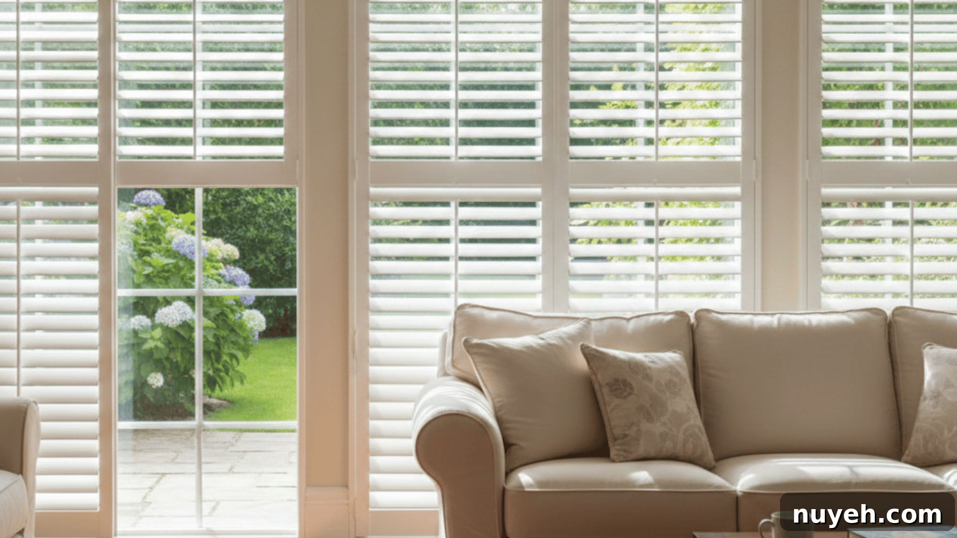 Shutters vs Blinds: Which Window Treatment Fits Your Home? 3 a bright living room with white plantation shutters, a beige sofa, and a wooden coffee table, overlooking a garden outside.