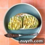 an avocado tartine sits on a blue plate with a vintage silver knife over a peach tile background.