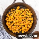 Cubed butternut squash in a skillet on a marble countertop.