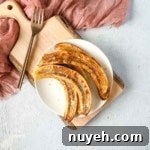 air fryer bananas on a white plate over a rustic wooden cutting board with a pink linen and a copper fork.