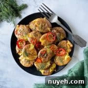 Smashed air fryer potatoes are shown dressed in lemon, rosemary, chili vinaigrette on a black plate with a green linen and a bunch of dill.