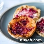Three English muffins with butter and jam sit on a blue plate.