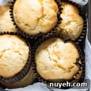A close-up of a baking tray holding five freshly baked muffins in paper liners. The muffins are golden brown and nestled in the tray on a parchment paper lining.