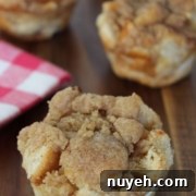 Four cinnamon crumb muffins are placed on a wooden surface, with a red and white checkered cloth partly visible to the left.