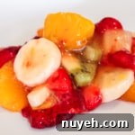 A plate of fruit salad with banana slices, strawberries, kiwi, and orange segments in a light syrup.