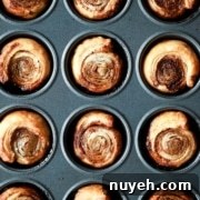 A muffin tin filled with twelve evenly-spaced, baked cinnamon rolls with golden-brown tops.