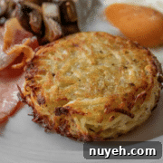 A close-up of a breakfast plate featuring a hash brown patty, a fried egg, mushroom pieces, and slices of bacon.