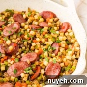 A pan with a colorful vegetable medley mixed with slices of sausage. The dish includes diced potatoes, carrots, and bell peppers, garnished with chopped parsley.