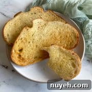 Three slices of toasted bread--one with a bite taken out of it--are shown on a white plate on a white marble counter.