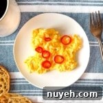 chilli scrambled eggs on a white plate surrounded by a cup of coffee, English muffins, and a copper fork.