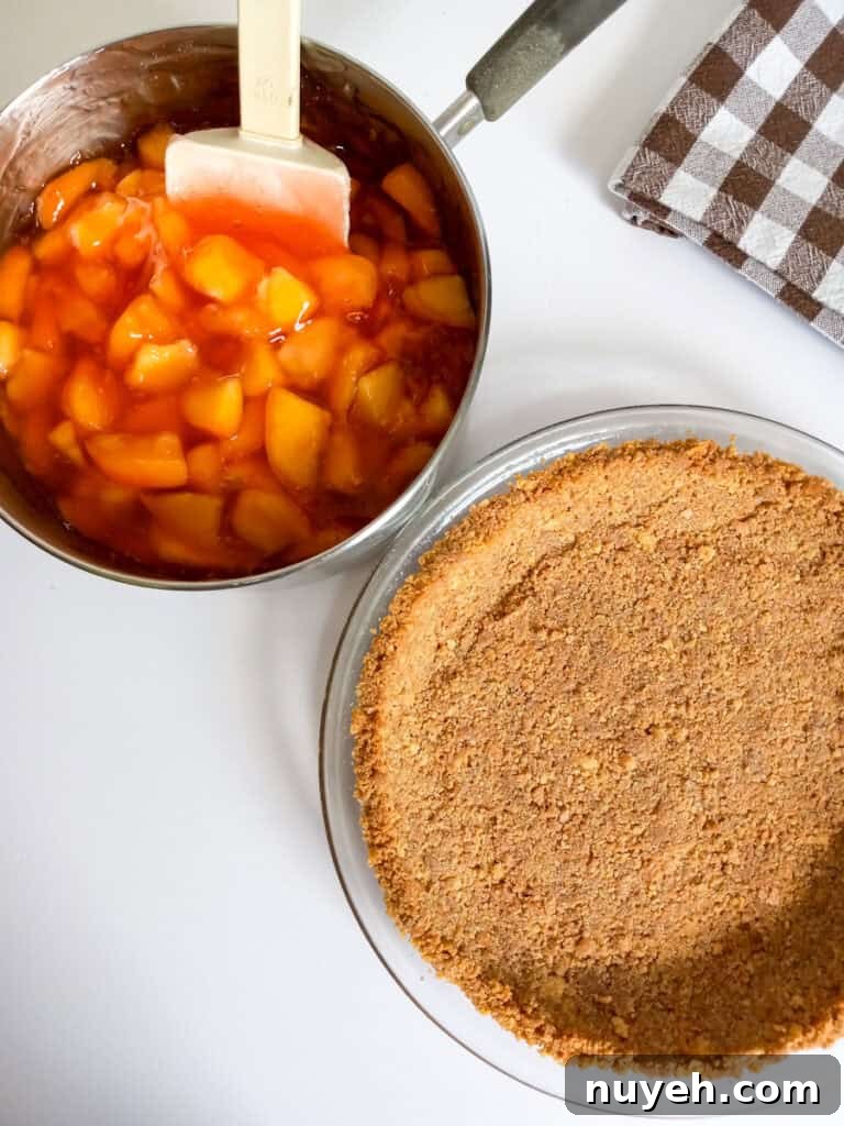sliced peaches and sauce in saucepan beside a graham cracker crust.