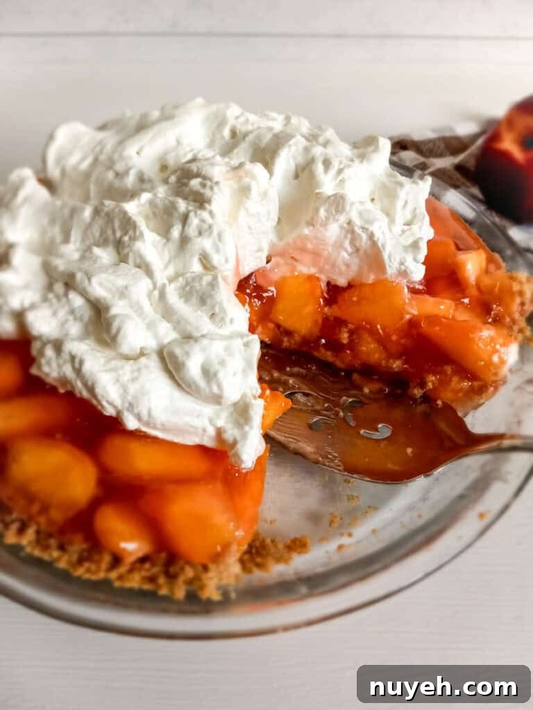 a whole Amish peach pie with graham cracker crust and whipped cream, with a slice removed.